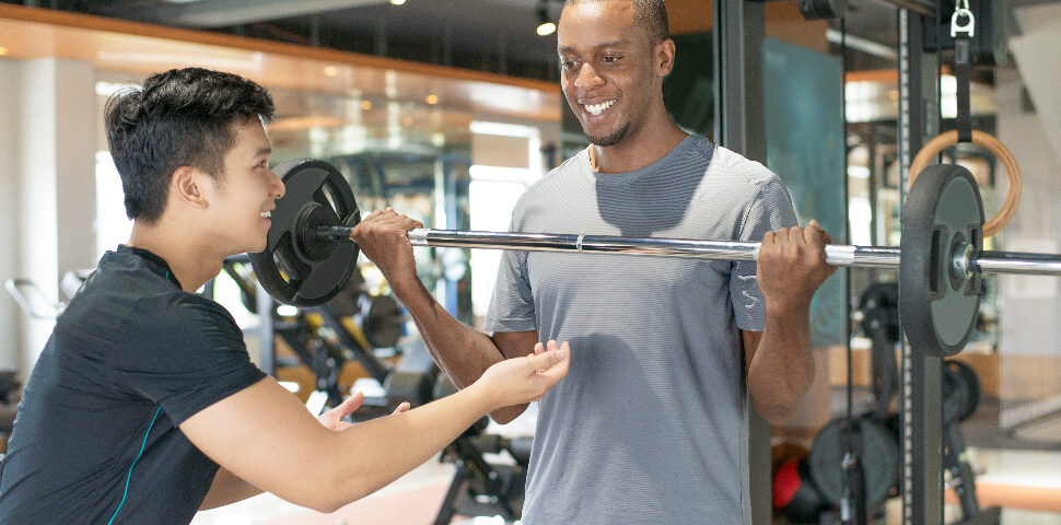 smiling black man lifting barbell with personal trainer 1
